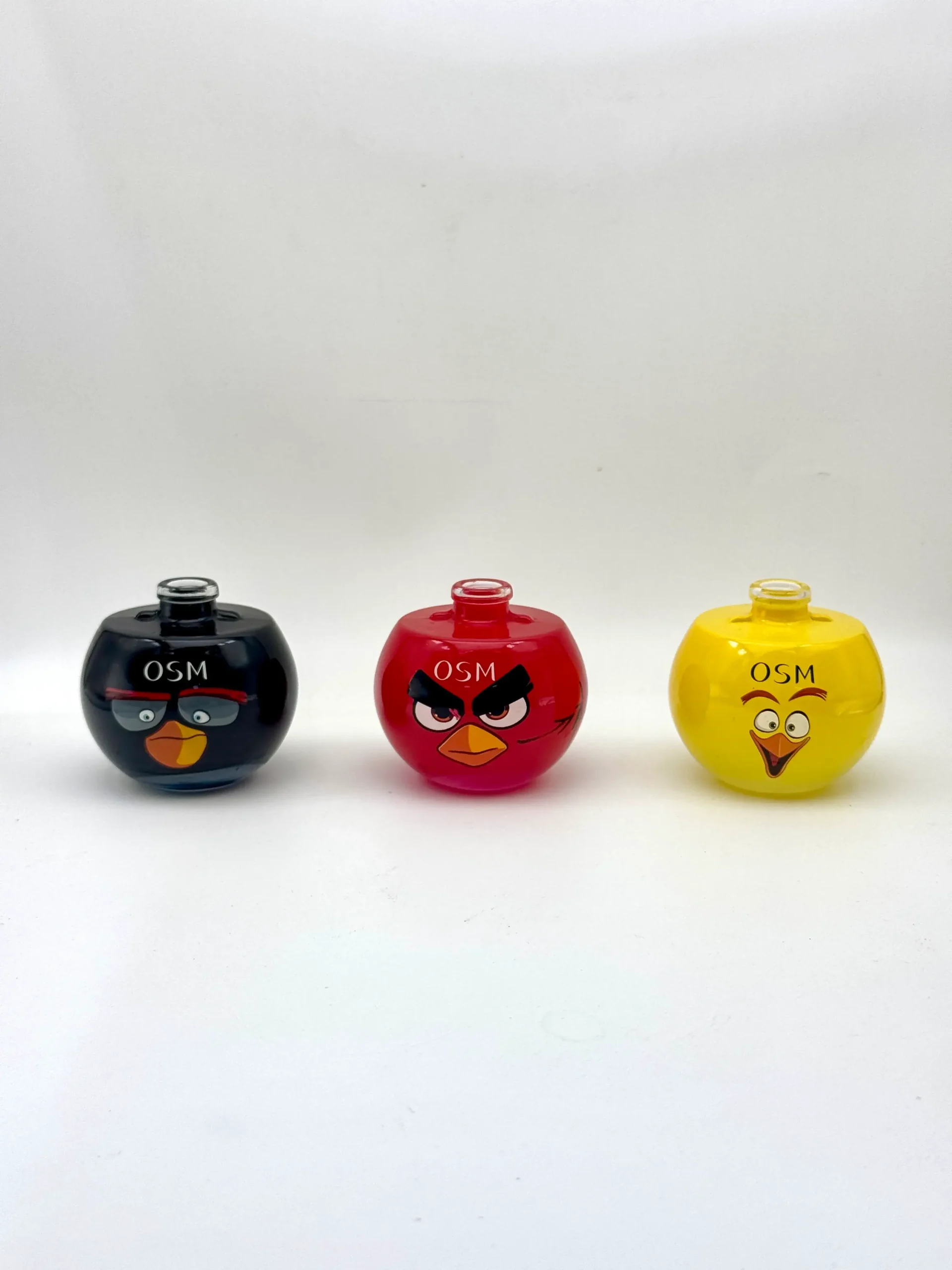 Three round character glass bottles in black, red and yellow with cartoon faces